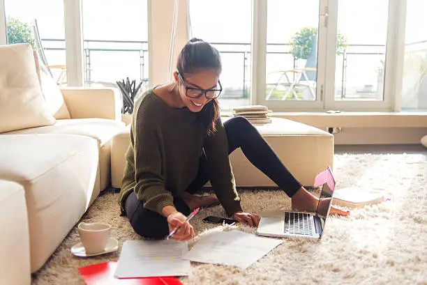 Photo of smiling young woman studying in her living room