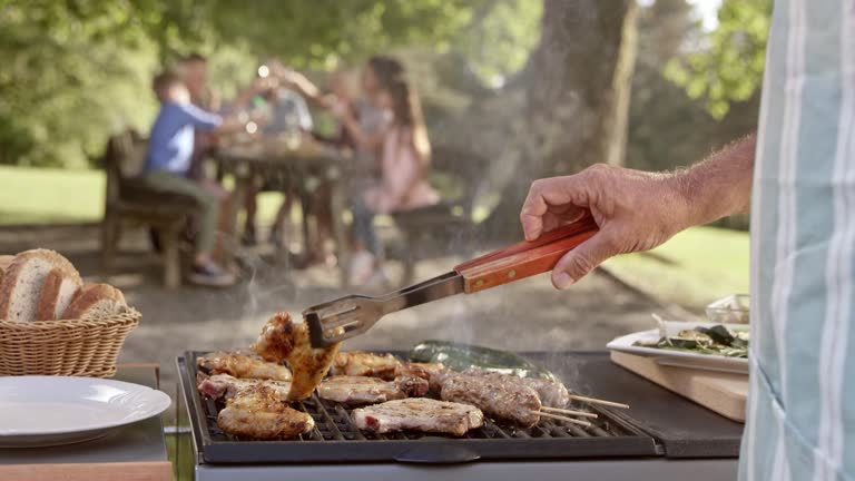 SLO MO Man flipping meat on the grill at a family picnic