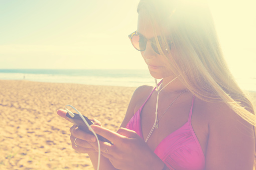 Young woman with phone and earphones at the beach in the sun