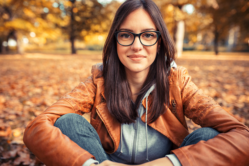 Portrait of young urban style woman sitting at park.Autumn season.