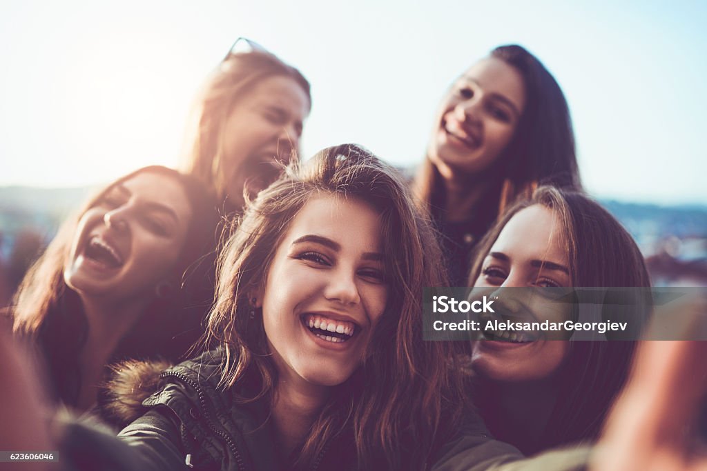 Grupo de garotas sorridentes tirando uma selfie ao ar livre ao pôr do sol - Foto de stock de Amizade royalty-free