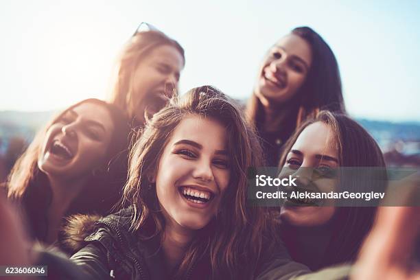 Foto de Grupo De Garotas Sorridentes Tirando Uma Selfie Ao Ar Livre Ao Pôr Do Sol e mais fotos de stock de Amizade