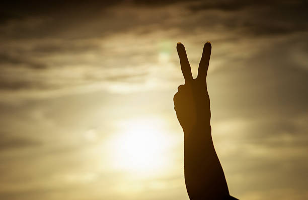 istock woman hand raising two fingers on sunset background 623612412
