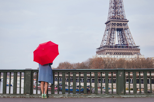 woman with red umbrella standing on the bridge with the view of Eiffel tower in Paris, France