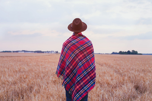 living rural, countryside style, man in hat covered in cozy checkered plaid standing in the field