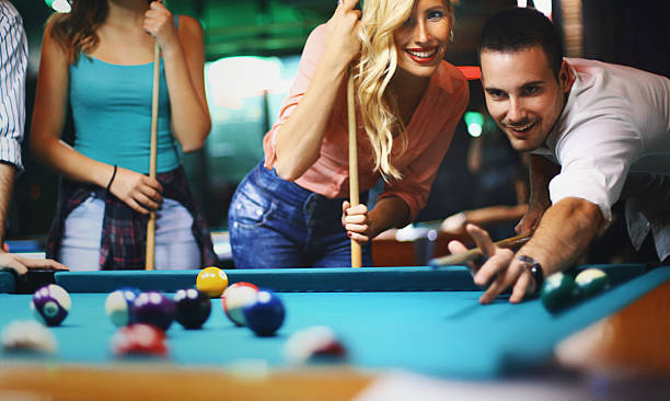 Friends shooting pool. Closeup front view of goup of mid 20's people shooting pool. There are two guys and two girls divided in two teams. One of the guys is on the move and his team mate is cheering while the other couple is hopping he misses. pool break stock pictures, royalty-free photos & images