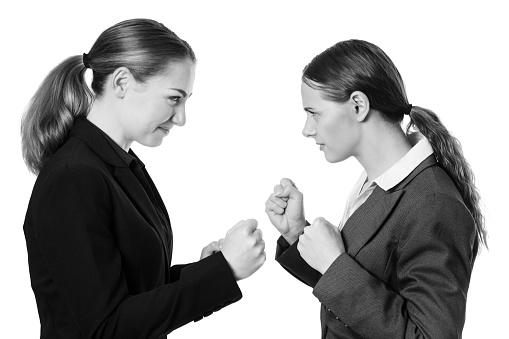 Studio shot of two business women with their fists raised, ready for a fight. Isolated on White.