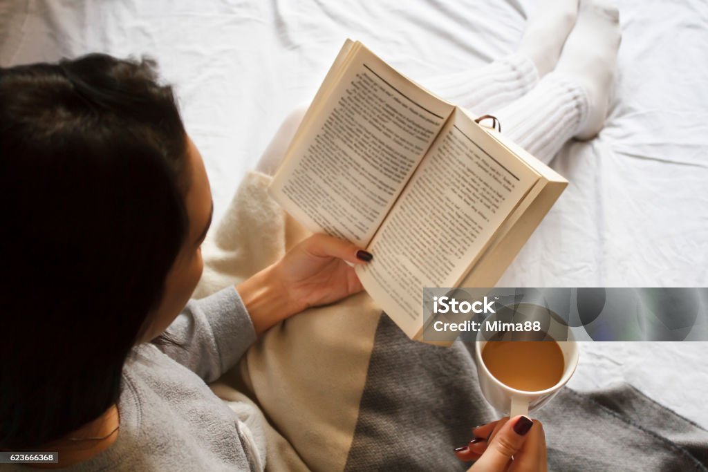 girl reading book and drinking coffee in bed in the morning beautiful brunette girl reading book and drinking coffee in bed in the morning Reading Stock Photo