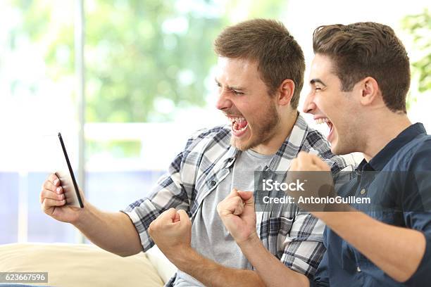 Excited Friends Watching Tv On A Tablet Stock Photo - Download Image Now - Sport, Downloading, Watching