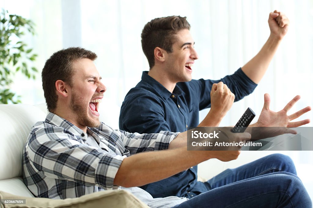 Compañeros de cuarto emocionados viendo la televisión en casa - Foto de stock de Compañero de vivienda libre de derechos