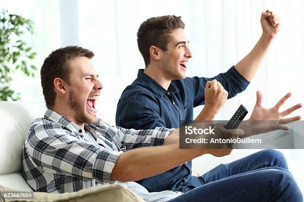 Compañeros De Cuarto Emocionados Viendo La Televisión En Casa Foto de stock y más banco de imágenes de Compañero de vivienda