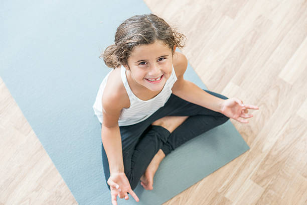 Young Girl Relaxing on the Mat An elementary age girl is meditating and doing yoga on an exercise mat. She is smiling and looking up at the camera. mindfulness kids stock pictures, royalty-free photos & images
