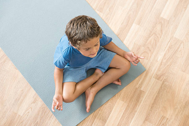Calm Child Meditating An elementary age boy is meditating on an exercise with his eyes closed. The picture is taken from overhead looking down at the child. mindfulness kids stock pictures, royalty-free photos & images