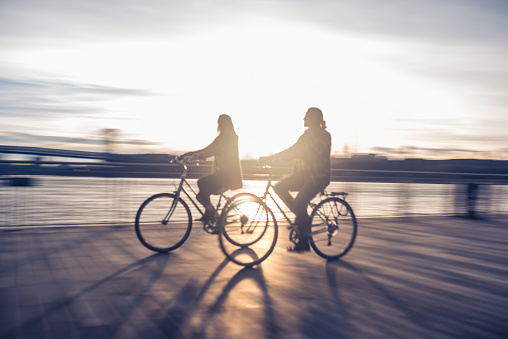 Young couple is cycling on a pier. They are looking at each other. New York in the back.