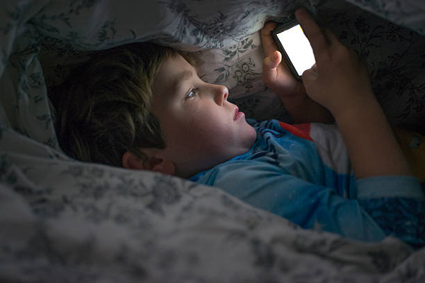 Young boy on cell phone under duvet stock photo