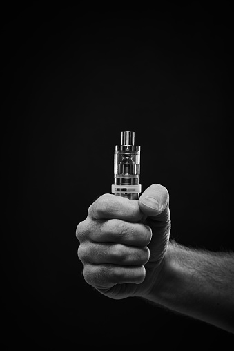 Black and white shot of young male hand holding tightly electronic cigarette against black background