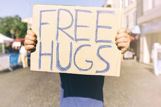 Free Hugs A man holds out a cardboard sign reading FREE HUGS, his face covered by the sign; it's a sunny summer's day. free hug stock pictures, royalty-free photos & images