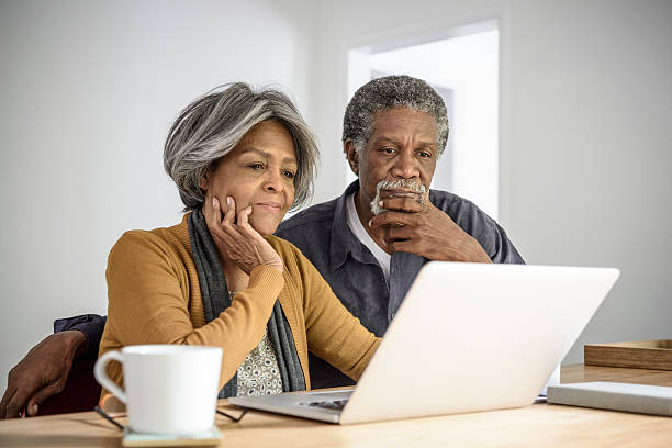 pareja afroamericana de la tercera edad usando la computadora portátil, contemplando - home finances couple computer african ethnicity fotografías e imágenes de stock