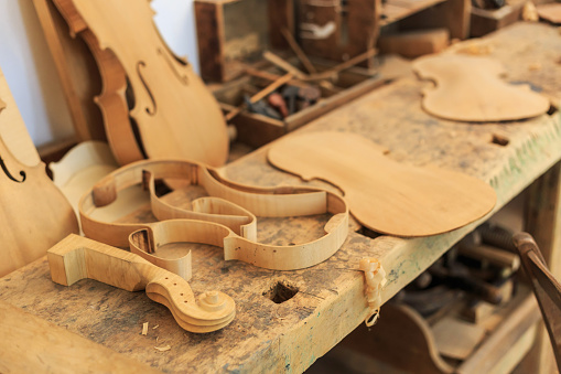 Unfinished violin in workshop. Tools and wooden parts around.