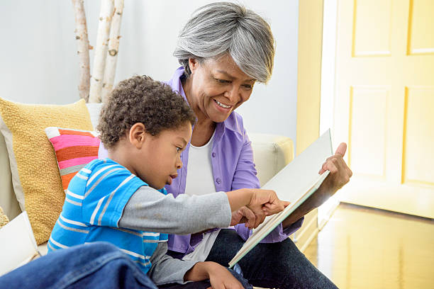 african american babcia pokazano książkę wnukowi, uśmiechnięty - grandmother reading child grandson zdjęcia i obrazy z banku zdjęć