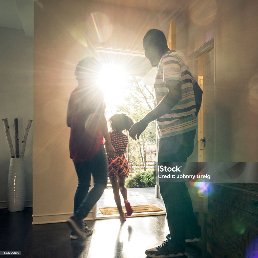 Parents with daughter leaving  the house in bright sunlight The young girl is running through the open front door and the mother and father are getting ready to leave Opening Stock Photo