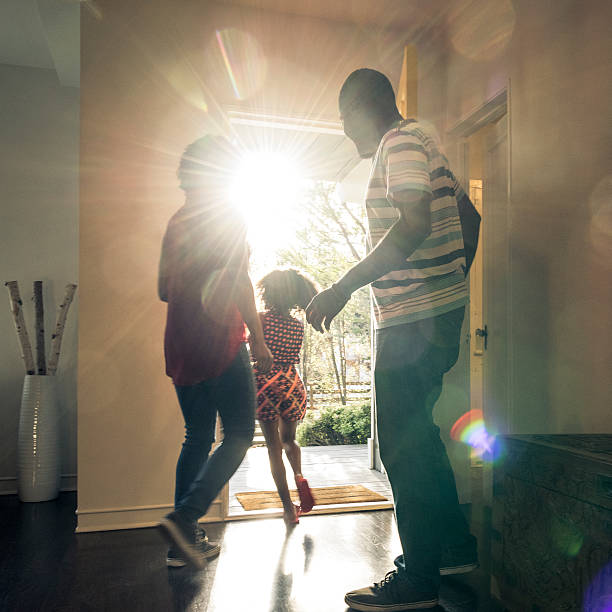 Parents with daughter leaving  the house in bright sunlight The young girl is running through the open front door and the mother and father are getting ready to leave opening stock pictures, royalty-free photos & images