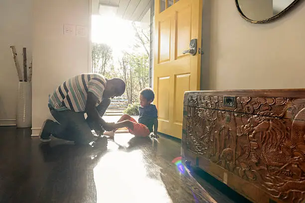 Photo of African American father helping son with shoes by front door