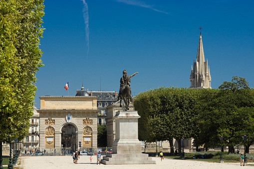 Montpellier, France - August 5, 2015: The Arc de Triomph in Montpellier viewed through trees on a treelined avenue with a statue in the foreground.