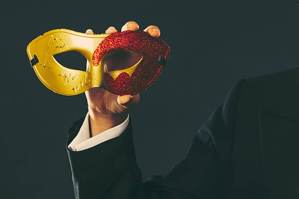 Holidays, people and celebration concept. Male hand holding red golden carnival mask closeup on dark