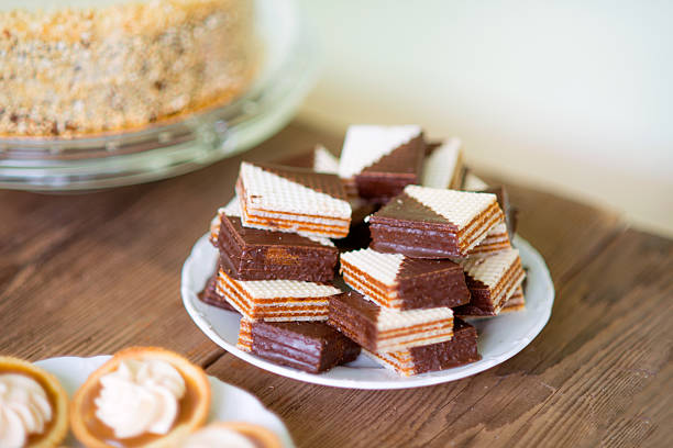 Close up, chocolate waffers and tarts filled with jam decorated with vanilla cream laid on plate. Studio shot. Wooden table backround.