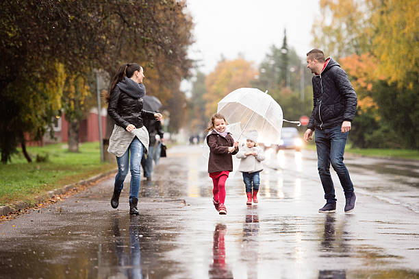 семья с дочерьми под зонтиками, бегая. дождливый день. - family fun running couple стоковые фото и изображения