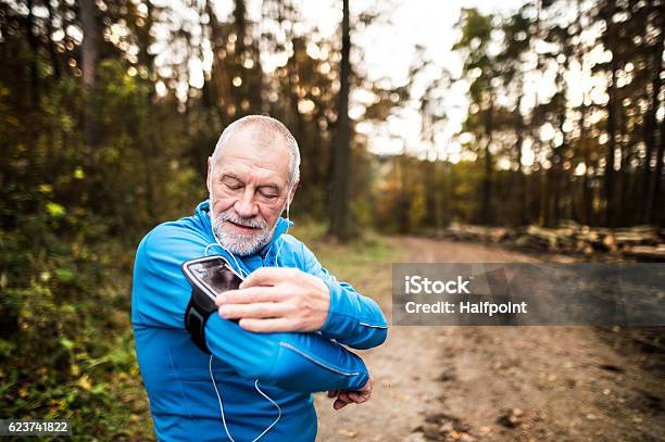 Corredor Senior En La Naturaleza Con Teléfono Inteligente Y Auriculares Foto de stock y más banco de imágenes de Tercera edad
