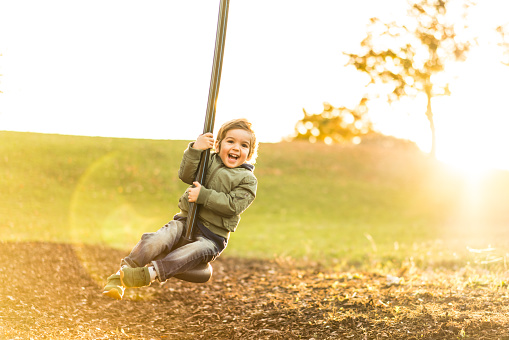 backlit image of cute three year old boy on a zip line in park