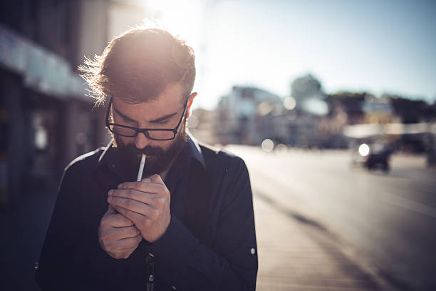 Hipster lighting a cigarette Young man lighting a cigarette on the street,front view smoking issues photos stock pictures, royalty-free photos & images