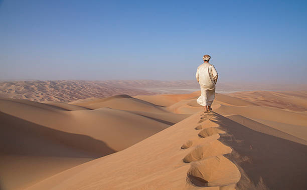 homme en kandura dans un désert au lever du soleil - oasis sand sand dune desert photos et images de collection
