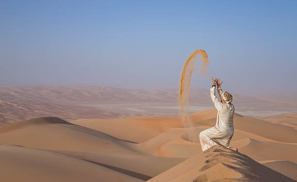 istock Man in kandura in a desert, throwing sand 623749020