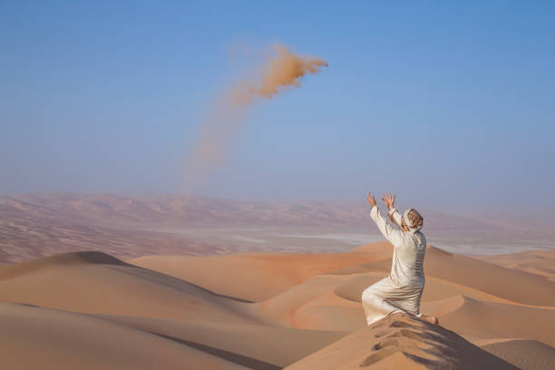 Man in traditional outfit in a desert at sunrise, throwing sand