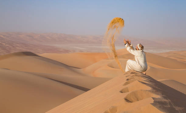 istock Man in kandura in a desert, throwing sand 623749046