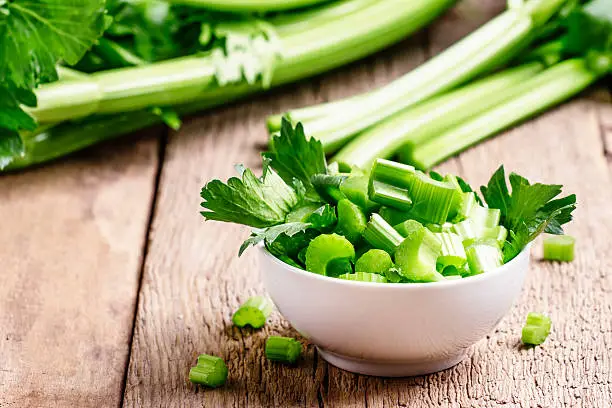 Fresh sliced celery in a white bowl on a vintage wooden background, selective focus