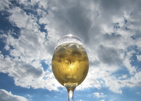 Copa de vino llena contra el cielo azul con nubes blancas photo