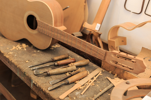 Unfinished acustic guitar in workshop. Tools and wooden parts around.