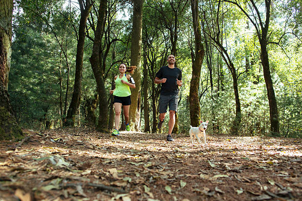 Cheerful couple running in the forest with dog