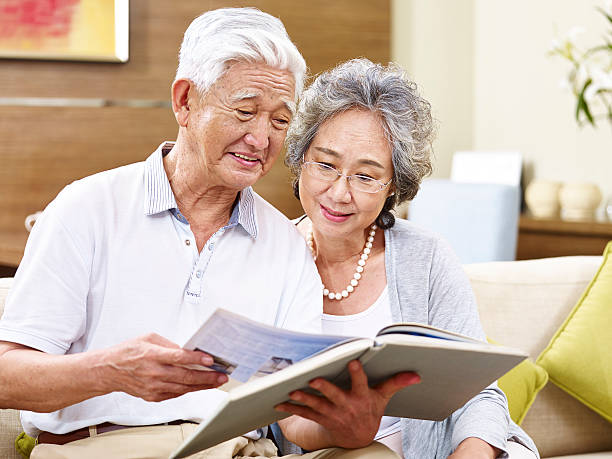senior asian couple reading a book together senior asian couple sitting on couch reading a book together hong kong 80s stock pictures, royalty-free photos & images