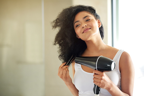Shot of an attractive young woman drying her hair with a hairdryer at home