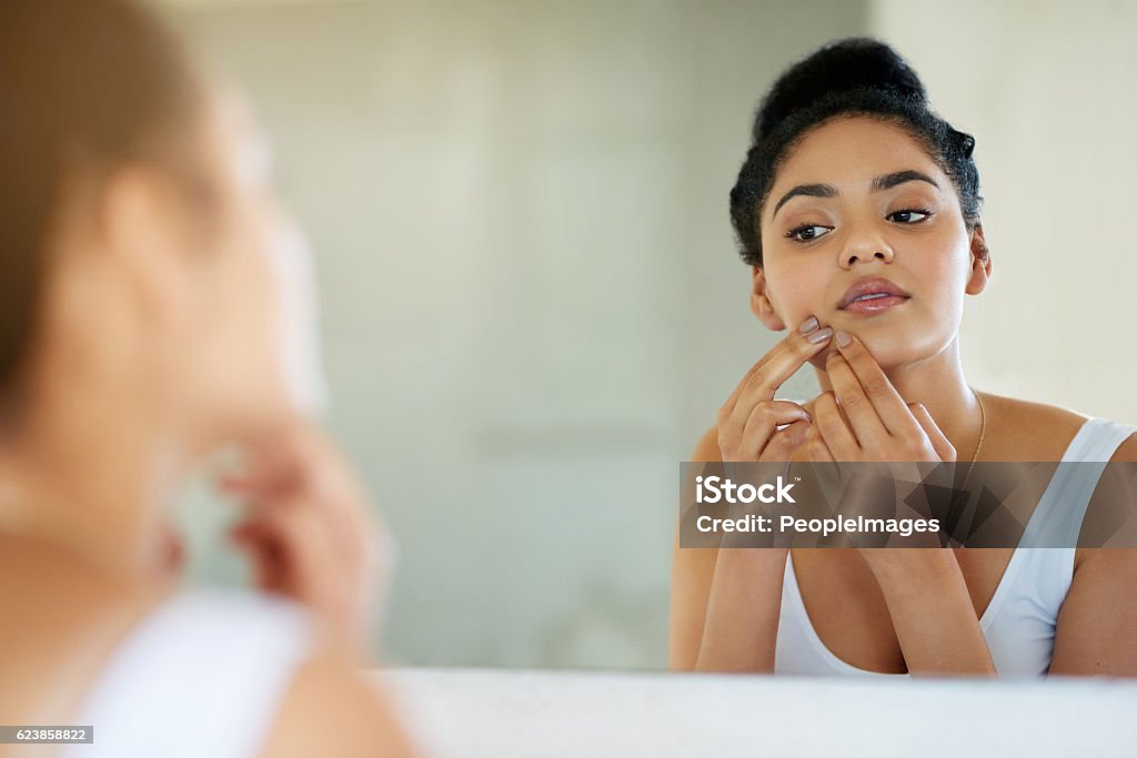 Her morning makeover Shot of a young woman inspecting her skin in front of the bathroom mirror Acne Stock Photo
