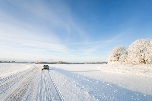 Small white hatchback car driving along a snowy winter road on a cold morning