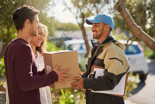 Shot of a courier delivering a package to a smiling young couple at home
