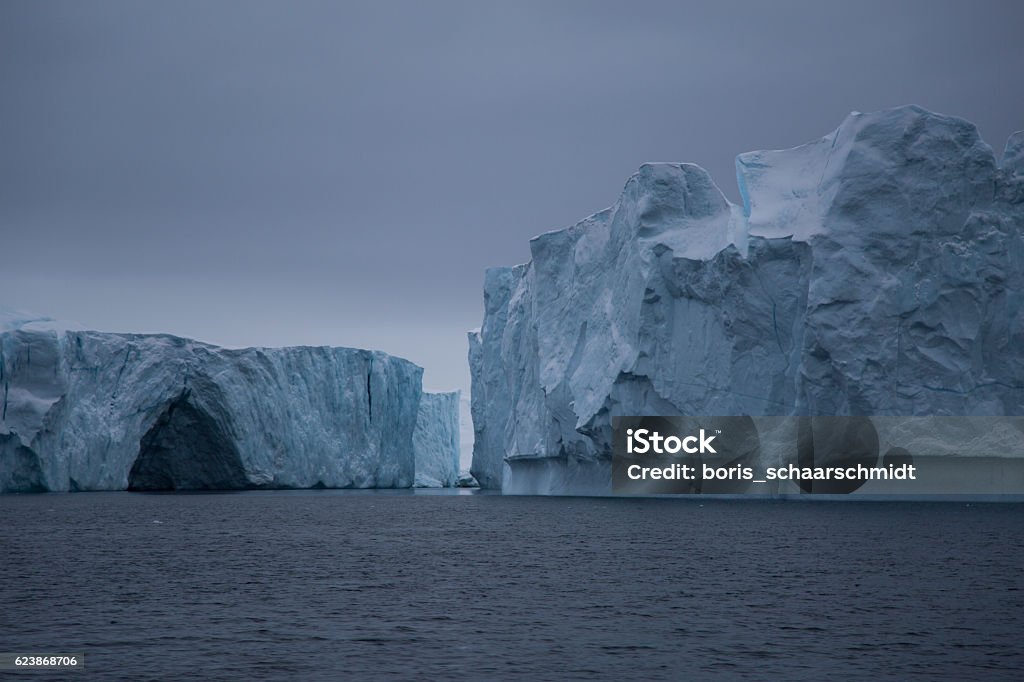 Two large icebergs with small cave Ilulissat Icefjord in Greenland Cave Stock Photo