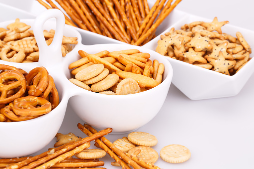 Different salted crackers in bowls on white background.