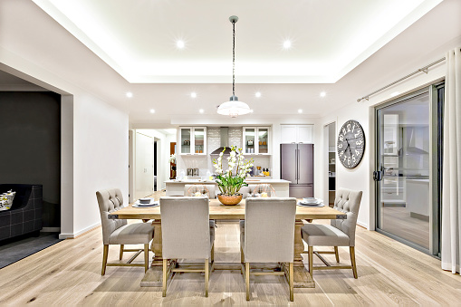 Modern dining room with hanging lamps on, there are chairs and table setup with fancy items on the wooden floor